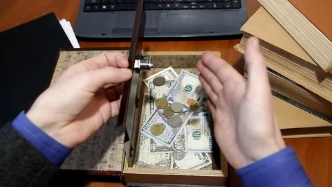 A man's hand opens a mini safe and lays coins over the banknotes, the top view Stock Footage 83247140