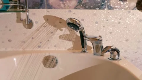 A man's hand opens a water tap to fill a white, modern, glossy bathtub Stock Footage 303174037