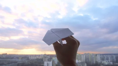 Man's hand with paper plane during sunset with cloudy sky on the city background Stock Footage 83708426