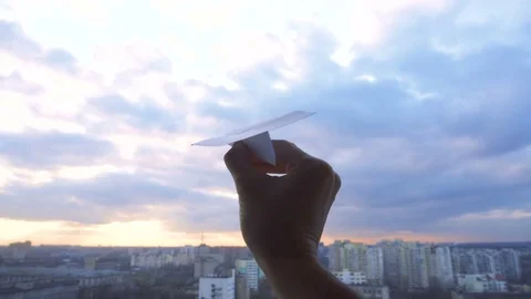 Man's hand with paper plane during sunset with cloudy sky on the city background Stock Footage 83784482