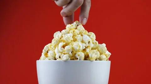 Man's hand picked the popcorn in the white bowl with red background Stock Footage 135668899