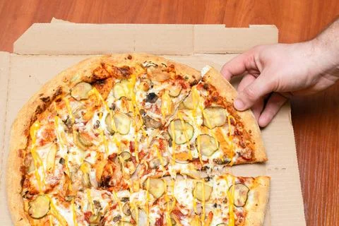 Man's hand picking slice of pizza with cheese, mushroom, meat, pickles, pep.. Foto stock