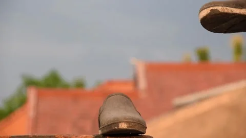 Man's hand picking up worn black shoes on brick rooftop in Indonesia Stock Footage 312055749