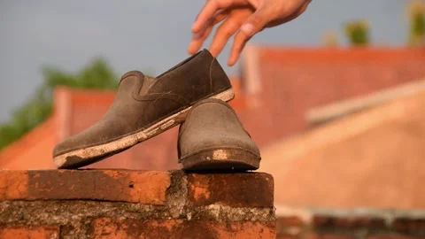 Man's hand picking up worn black shoes on brick rooftop in Indonesia Stock Footage 312056130