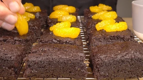Man’s hand placing mandarin pieces on chocolate brownies. Stock Footage 104040089
