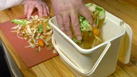 Man's hand placing raw vegetable waste into a small composting bin. Stock Footage 171421138
