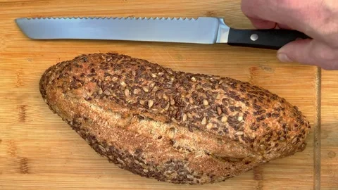 A man’s hand placing an uncut bread loaf and a knife on a cutting board. Vídeos de archivo 251568755