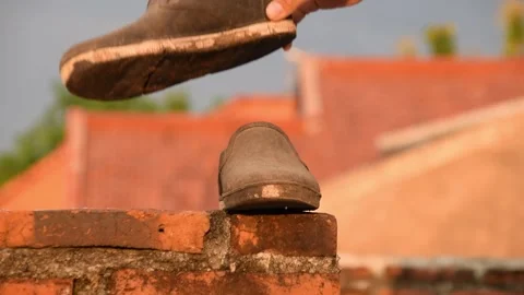 Man's hand placing worn black shoes on brick rooftop wall in Indonesia Stock Footage 312056024