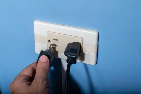 Man's hand plugging in a black wire. Latin, Colombian electrical outlet. Stock Photos