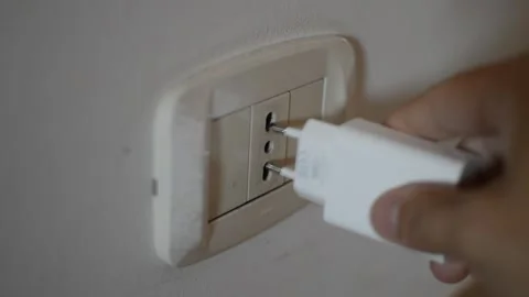 Man's hand pluging white charger cable to a europea wall soket Stock Footage 197950984