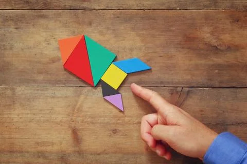 Man's hand pointing at rocket made from square tangram puzzle Foto stock