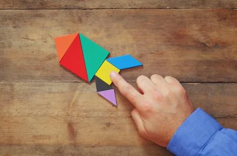 Man's hand pointing at rocket made from square tangram puzzle Stock Photos
