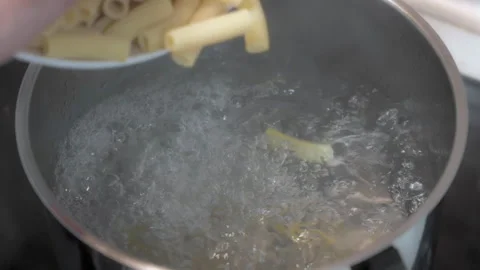 Man's hand pouring macaroni pasta into a pot of boiling water to be cooked Video stock 252489705