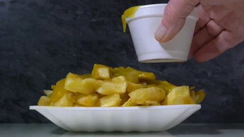 A man's hand pouring thick curry sauce over a pile of takeaway chips. Video stock 150106817