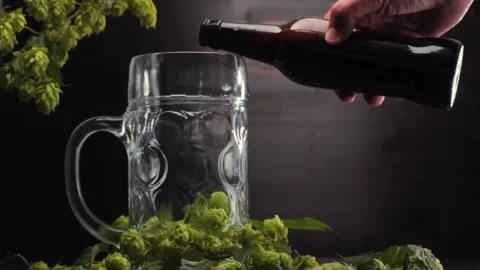 Man's hand pours beer from a bottle into a beer glass on a wooden background Stock Footage 221545170