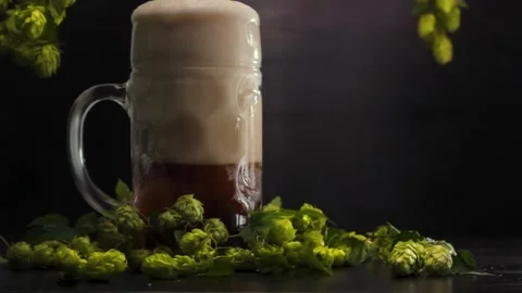 Man's hand pours beer from a bottle into a beer glass on a wooden background Stock Footage 221545209