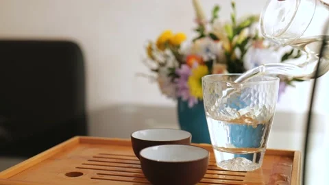 Man's hand pours brewed white tea from a small glass teapot into a glass cup. Stock Footage 220341929