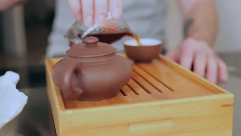 A man's hand pours tea from a chahai into a bowl. man pouring pu-erh tea Stock Footage 218448052
