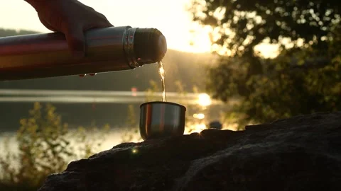 A man's hand pours tea from a thermos into a mug at sunset Stock Footage 247923090