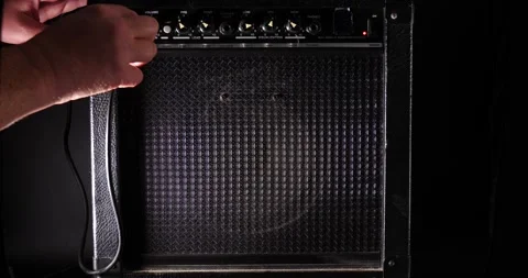 Man's hand powering on guitar amplifier plugging microphone in isolated on black Stock Footage 204959830