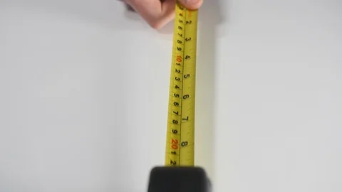 Mans hand pulling an industrial yellow metal tape measure against a white Stock Footage 88507575