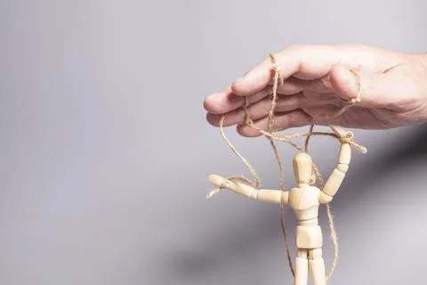 Man's hand pulling strings of wooden puppet on gray background. Concept of em Stock Photos