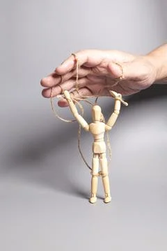 Man's hand pulling strings of wooden puppet on gray background. Concept of .. Stock Photos