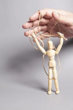 Man's hand pulling strings of wooden puppet on gray background. Concept of .. Stock Photos