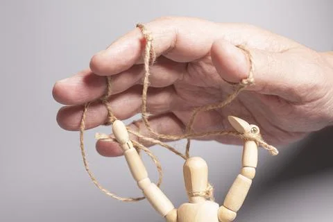 Man's hand pulling strings of wooden puppet on gray background. Concept of .. Stock Photos