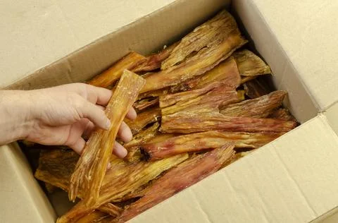 A man's hand pulls Dried Beef Tendon out of a cardboard box. Stock Photos