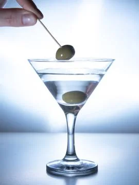 A man's hand pulls an olive on a skewer from a glass of water Stock Photos