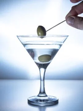 A man's hand pulls an olive on a skewer from a glass of water Stock Photos