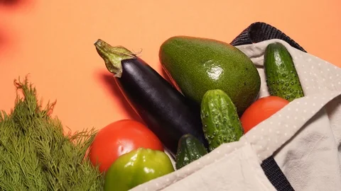 The man's hand pulls out a fresh avocado from a cotton bag on a peach background Видео 125770769