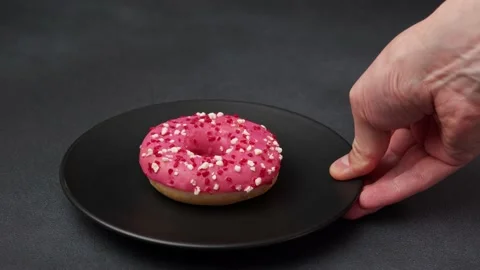 A Man's hand Puts a black plate with a Pink Glazed Doughnut on the table Stock Footage 237300758