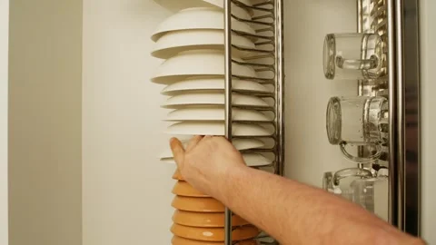 A man's hand puts clean dishes in a cupboard in the kitchen. Video stock 282276830