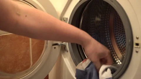 A man's hand puts dirty clothes in the washing machine, homework Stock Footage 157367110