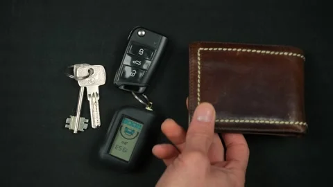 A man's hand puts down his house keys, car keys, and a brown wallet on the table Stock Footage 297398179
