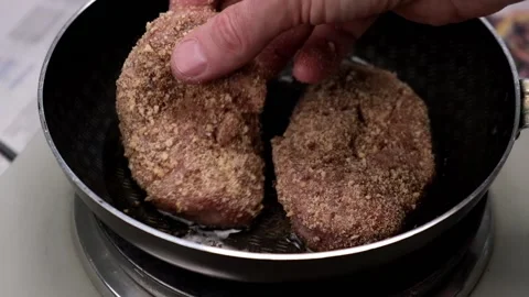A man's hand puts a fresh juicy cutlet in breadcrumbs on a frying pan. close-up. Stock Footage 174557588