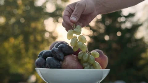 A man's hand puts fruit in a plate on the background of the sun's rays. Stock Footage 217798013