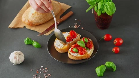 Man's hand puts grilled tomatoes on Bruschetta with Ricotto Cheese Stock-Footage 238468566