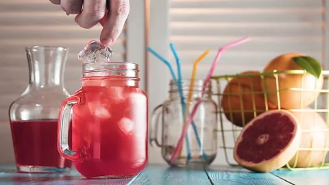 Man's hand puts ice cubes into grapefruit juice and inserts drinking straw. Stock Footage 87388406