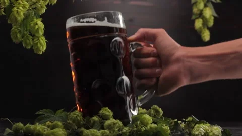 A man's hand puts a large glass of beer on a black background with hops Stock Footage 221546265