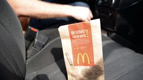 The man's hand puts the package from McDonald's into the front seat of the car Stock Footage 87453125