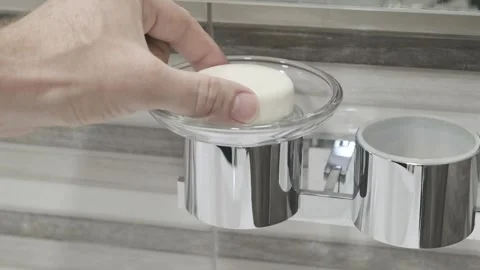Man's hand puts piece of round soap in glass soap dish Stock Footage 271069306