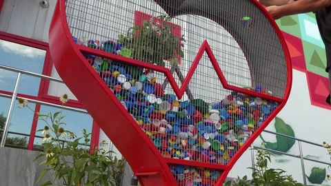 A man's hand puts plastic bottle caps into a Heart shaped recycling bin Stock Footage 211306475