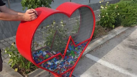 A man's hand puts plastic bottle caps into a Heart shaped recycling bin Stock Footage 211306728