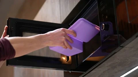A man's hand puts a plastic container with food in the microwave. Stock Footage 234128939