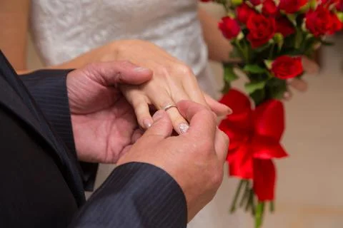 A man's hand puts a ring on his bride during the marriage ceremony. The girl is Stock Photos