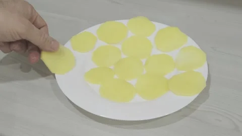 Man's hand puts sliced raw potatoes on plate for making chips Video stock 271069914
