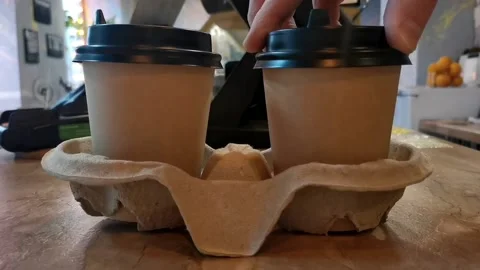 A man's hand puts two paper cups with coffee in a cup holder. Video stock 221170244